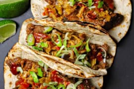 An overhead view of three Korean beef tacos with kimchi pressed against each other and topped with Korean bbq sauce and slivers of green onions.