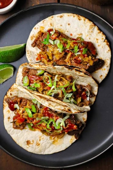 An overhead view of three Korean beef tacos with kimchi pressed against each other and topped with Korean bbq sauce and slivers of green onions.