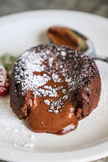 A straight-on view of a chocolate lava cake that has been cut into revealing the gooey chocolate interior.