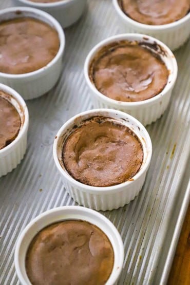 An overhead view of two rows of ramekins that are filled with baked chocolate lava cakes.