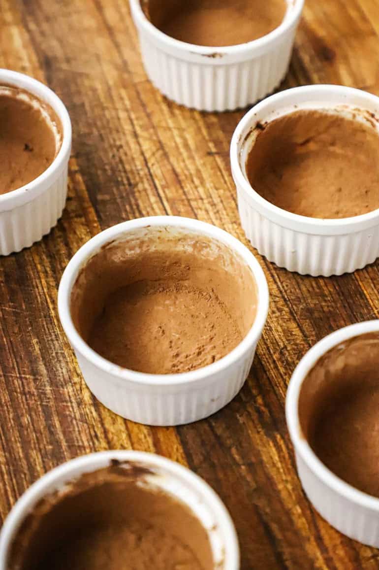 An overhead view of a six small ramekins that have been greased with butter on the inside and then dusted with cocoa powder.