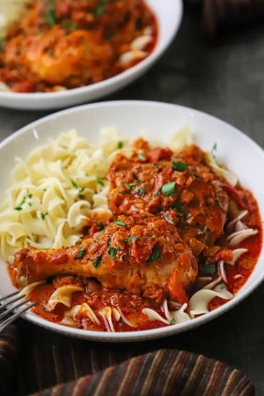 A straight-on view of two shallow white bowls filled with a serving of chicken paprikash over cooked egg noodles.