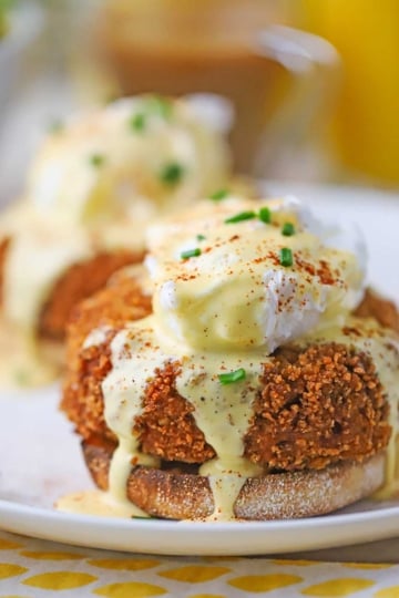 A close-up view of an untouched crab cakes egg Benedict with hollandaise flowing over the top of the poached egg and pooling on a white plate.