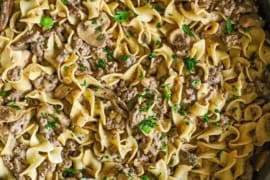 An overhead view of a large straight-edge stainless steel skillet filled with weeknight stroganoff of a creamy ground beef sauce tossed with egg noodles.