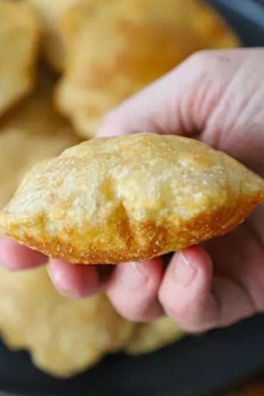 A close-up view of a person holding a puffy Indian fried bread poori in his hand over a black circular platter holding more poori.