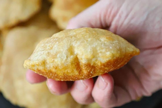 A close-up view of a person holding a puffy Indian fried bread poori in his hand over a black circular platter holding more poori.