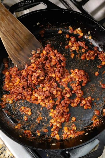 An overhead view of chopped onion that has been sautéed in a large black non-stick skillet and then blended with Hungarian paprika. 