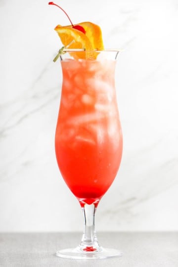 A straight-on view of a hurricane cocktail with an slice of orange and a maraschino cherry resting on top of the classic glass.