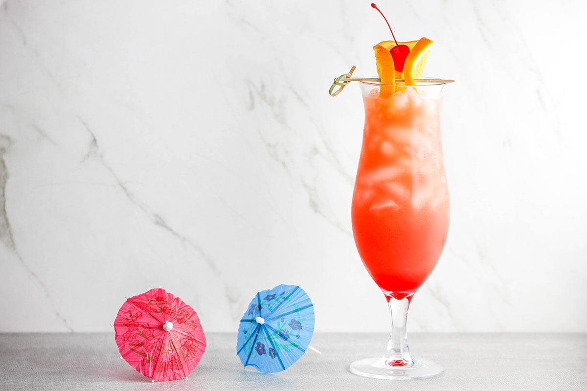 A straight-on view of a hurricane cocktail with a two drink umbrellas sitting nearby.