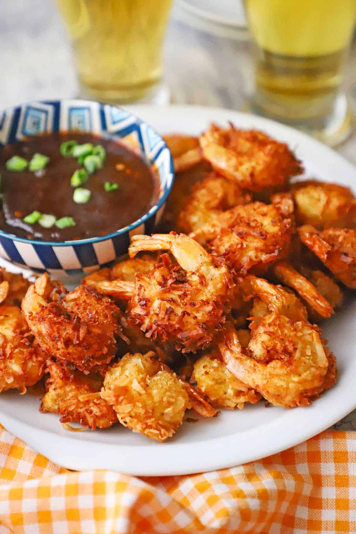 A straight-on view of a pile of crispy coconut shrimp on a white plate with a colorful bowl of Thai sweet chili sauce sitting next to the shrimp.