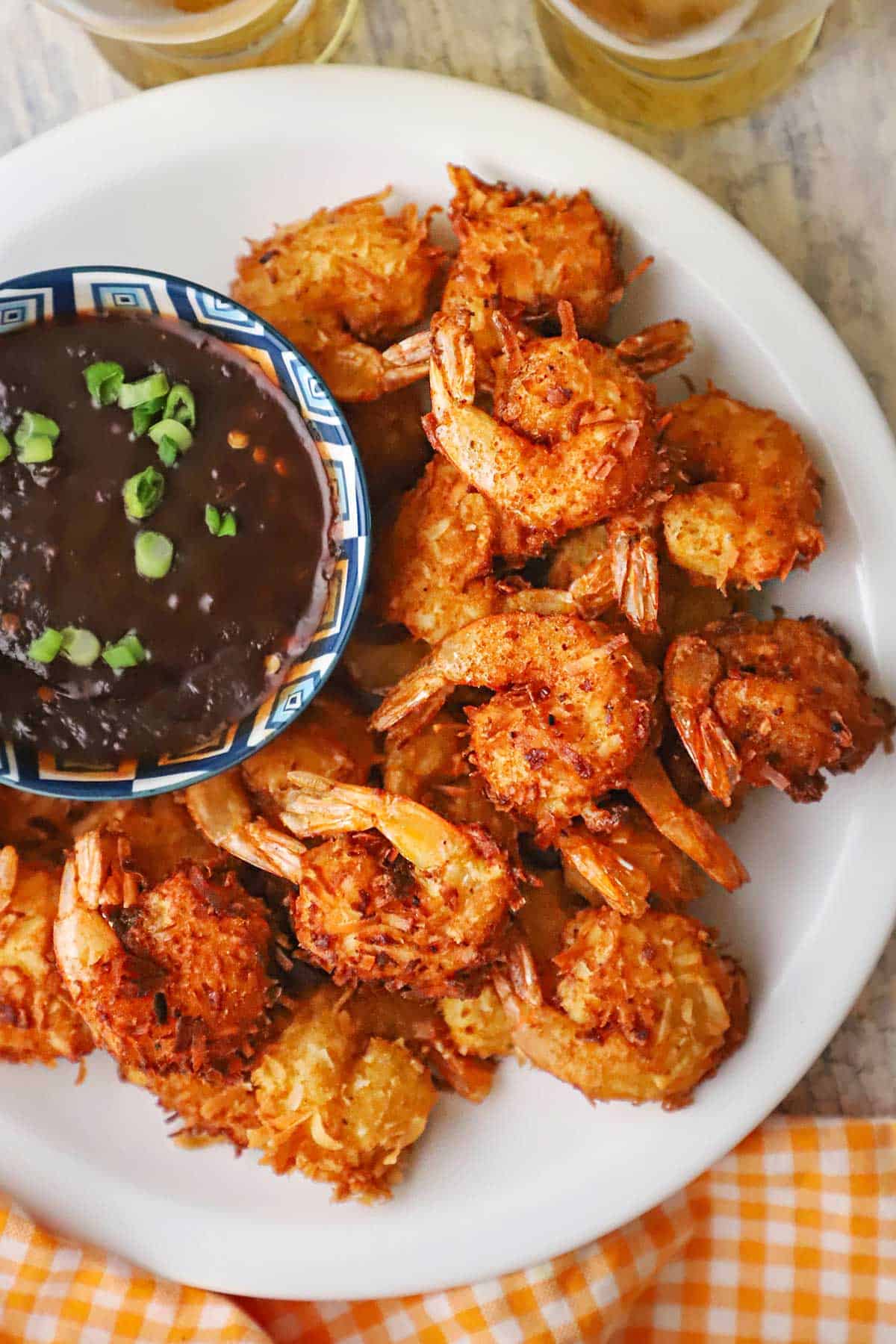 An overhead view of a white plate filled with a pile of crispy coconut shrimp resting next to a white and blue bowl filled with a thick Thai sweet chili sauce.