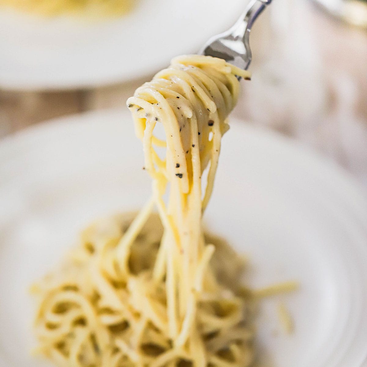 A person using a fork to raise a serving of tonnarelli cacio e pepe out of a bowl of the same. 