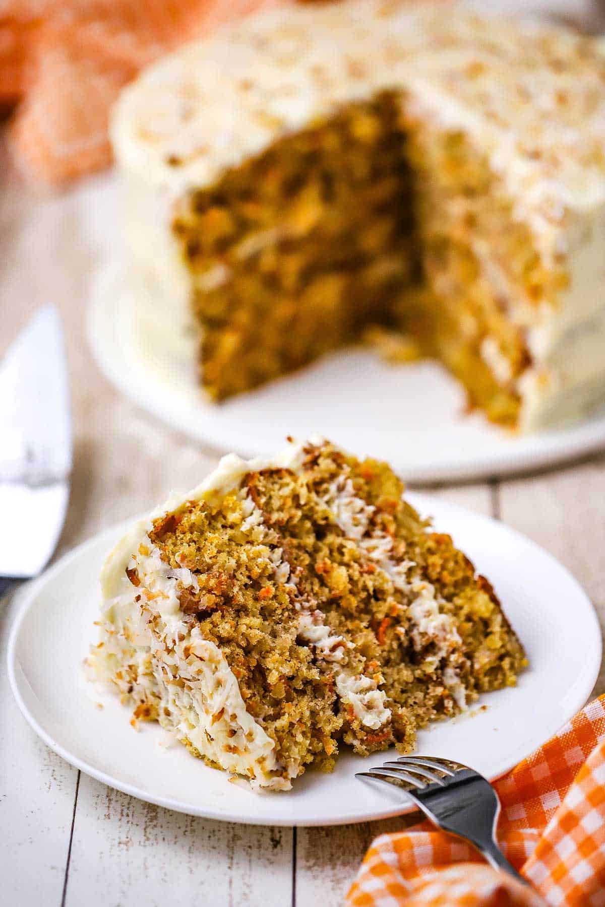 A slice of carrot cake with coconut and macadamia nuts sitting on its side on a white dessert plate. 