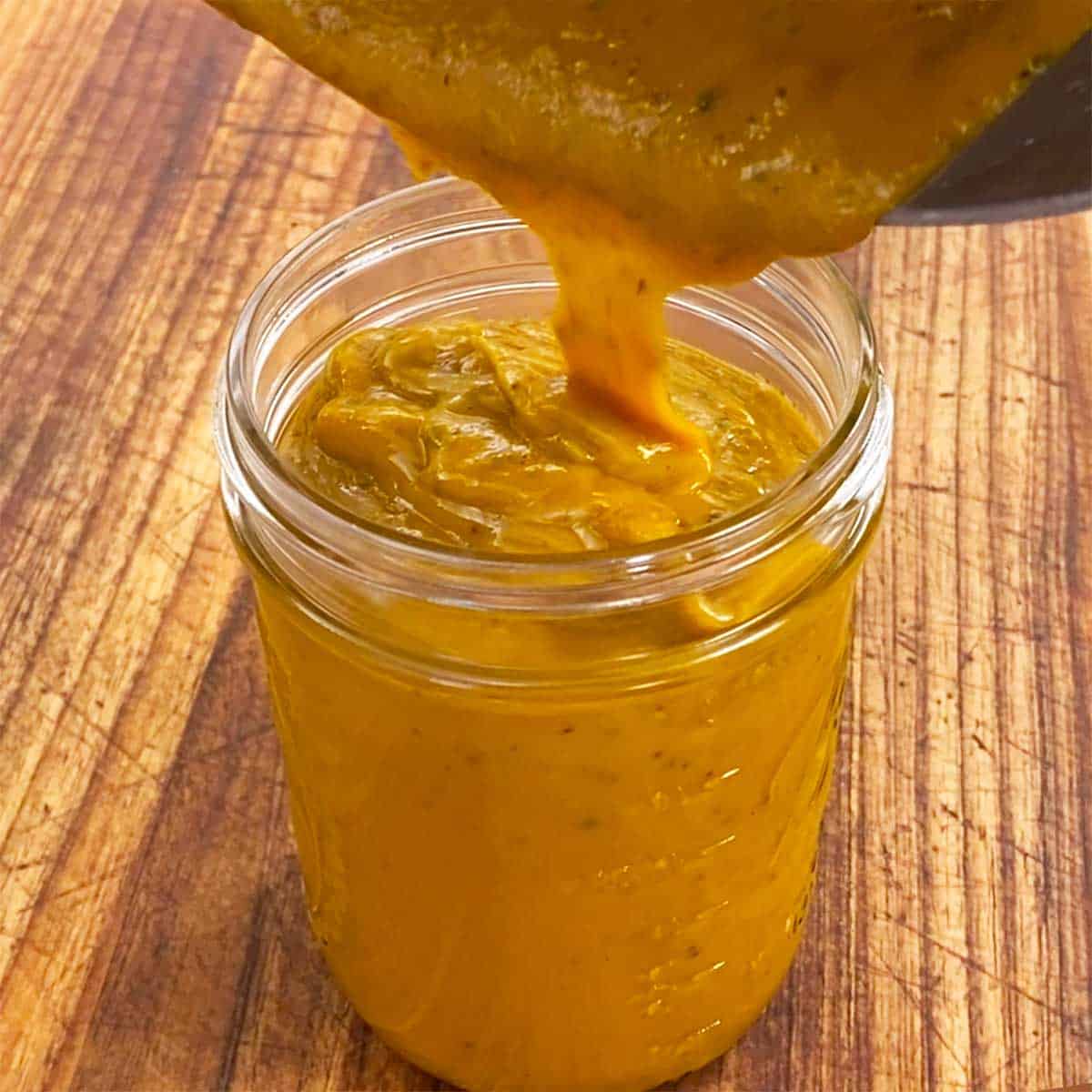 Carolina mustard sauce being poured from a saucepan into a glass jar on a cutting board. 