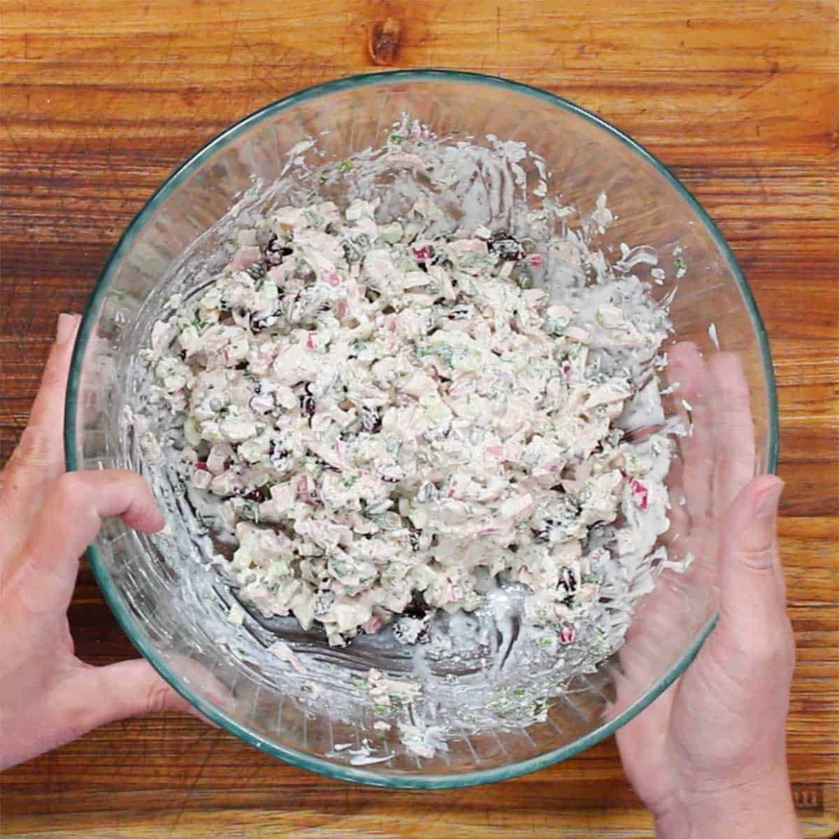 A person holding a glass bowl filled with best-ever tuna salad on a wooden cutting board. 