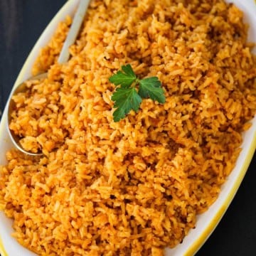 A platter filled with a pile of homemade Mexican rice topped with a sprig of fresh parsley.