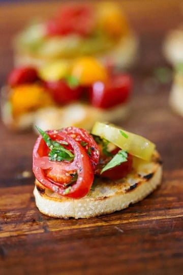 A single serving of Summer bruschetta with tomato and basil resting on a wooden cutting board.