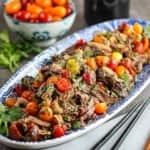 A long, blue and white oval platter filled with a large serving of Thai beef salad with two chopsticks nearby.