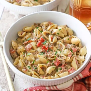 A close-up view of a white pasta filled with a serving of creamy beef and shells with a red-checkered napkin nearby.