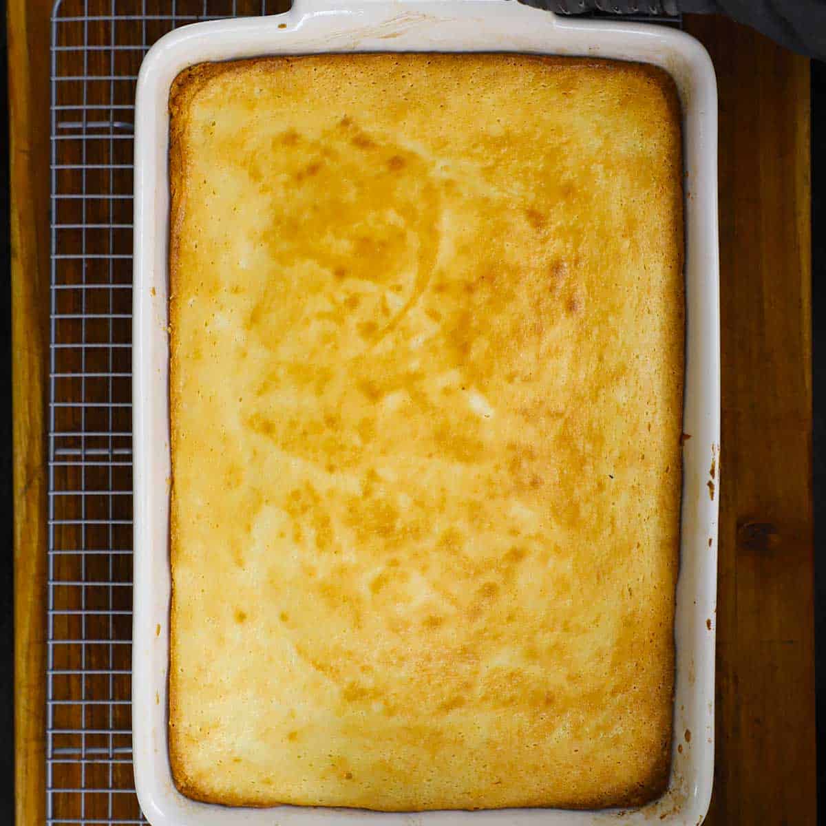 An overhead view of a fully baked Gooey Butter Cake in a white 9 by 13 inch baking dish resting on a baking rack.