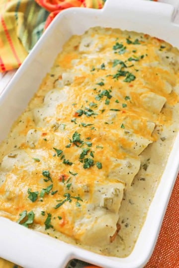 A nine by thirteen inch white casserole dish filled a row of chicken enchiladas with sour cream sauce.