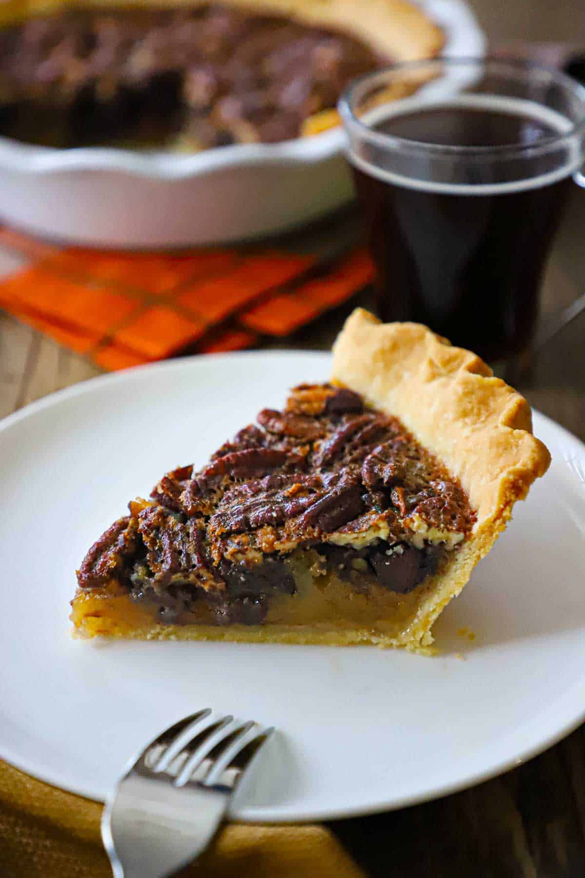 A slice of the best chocolate bourbon pecan pie on a white dessert plate with a fork off to the side.