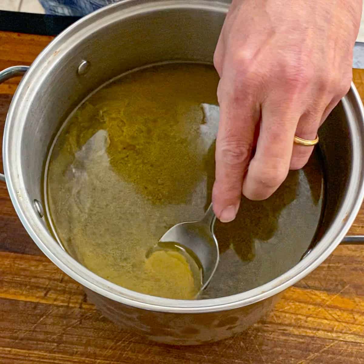 A person using a large spoon to scrape congealed fat from the surface of a stock pot filled with homemade roasted turkey stock.
