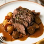 A white dinner plate filled with a serving of the best slow cooker pot roast with vegetables and brown gravy.
