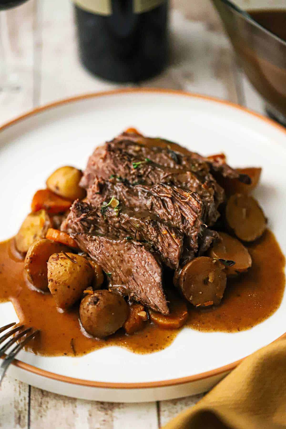 A white dinner plate filled with a serving of the best slow cooker pot roast with vegetables and brown gravy.