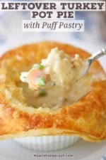 A person using a fork to raise the filling from the inside of an opened up leftover turkey pot pie with buttery puff pastry.