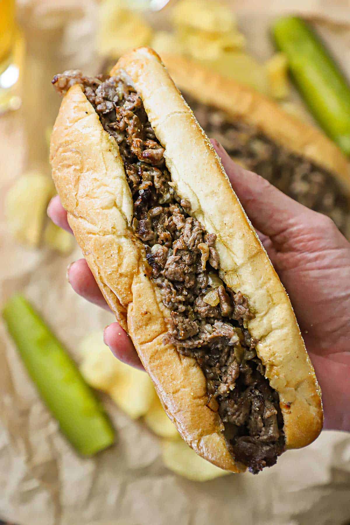 A person holding an uneaten, freshly prepared homemade Philly cheesesteak in his hand.