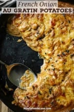 An overhead view of a black cast-iron skillet filled with French onion au gratin potatoes with a portion of the dish missing.