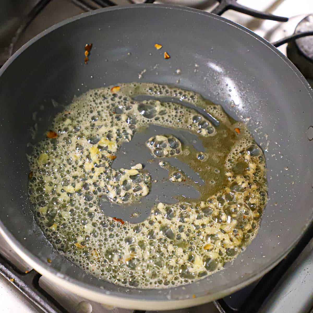 A large non-stick skillet holding simmering browned butter that has minced garlic being sautéed in it.