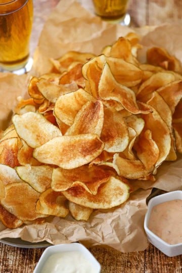 A close-up view of a large platter of crispy homemade potato chips with two small bowls of dipping sauce nearby.