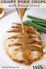A crispy pan-fried pork chop that has been sliced into strips on a plate with brown gravy being poured over it from someone holding a gravy boat.