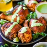 A close-up view of Authentic Peruvian Chicken with Green Sauce on a platter with a small white bowl of the sauce nestled nestled into the chicken pieces.
