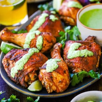 A close-up view of Authentic Peruvian Chicken with Green Sauce on a platter with a small white bowl of the sauce nestled nestled into the chicken pieces.
