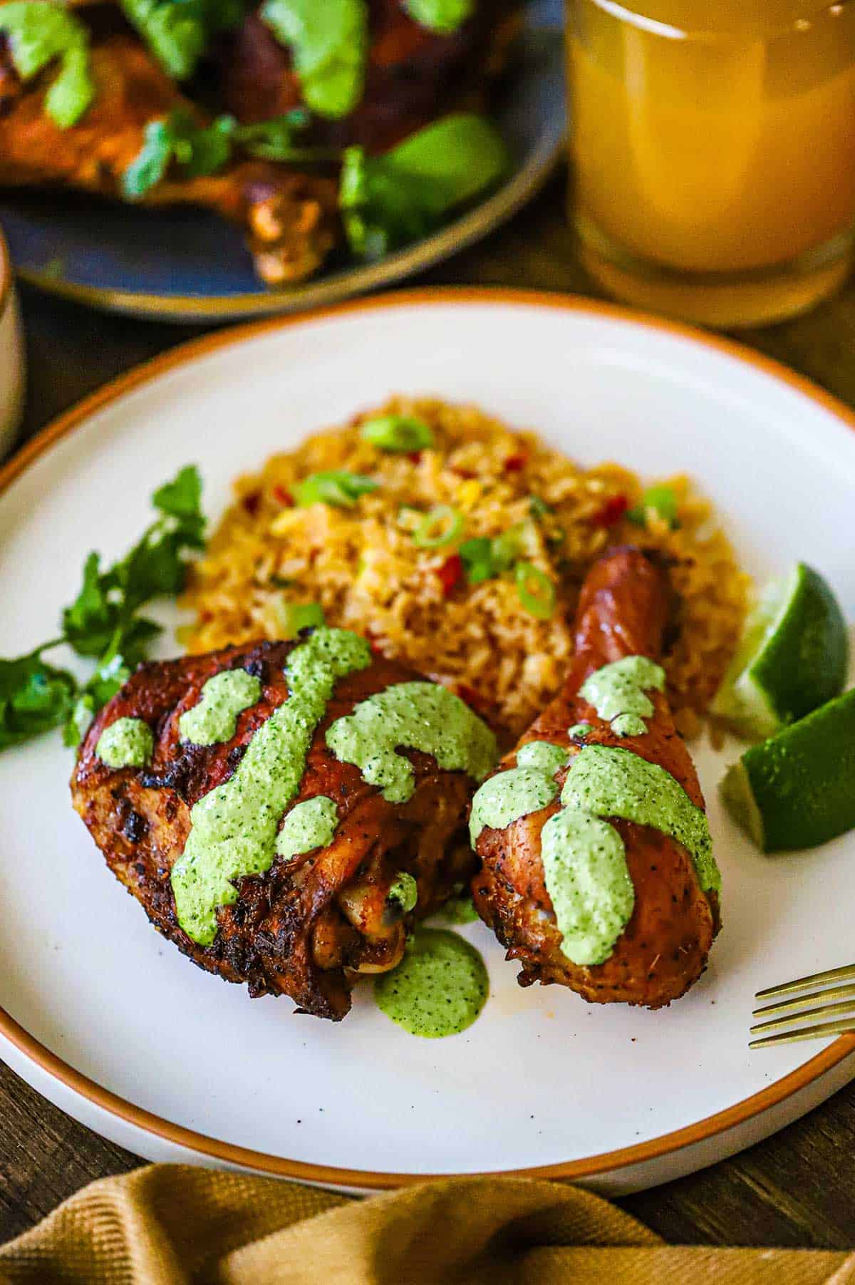 A white dinner plate filled with two pieces of Authentic Peruvian Chicken topped with a green sauce and next to a side of Peruvian Fried Rice (Arroz Chaufa).