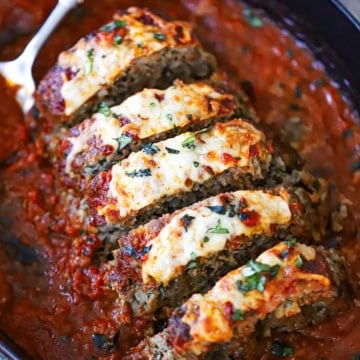 A close-up view of The Best Juicy Italian Meatloaf with Marinara Glaze that has been cut into slices and is resting in marinara sauce in a baking dish.