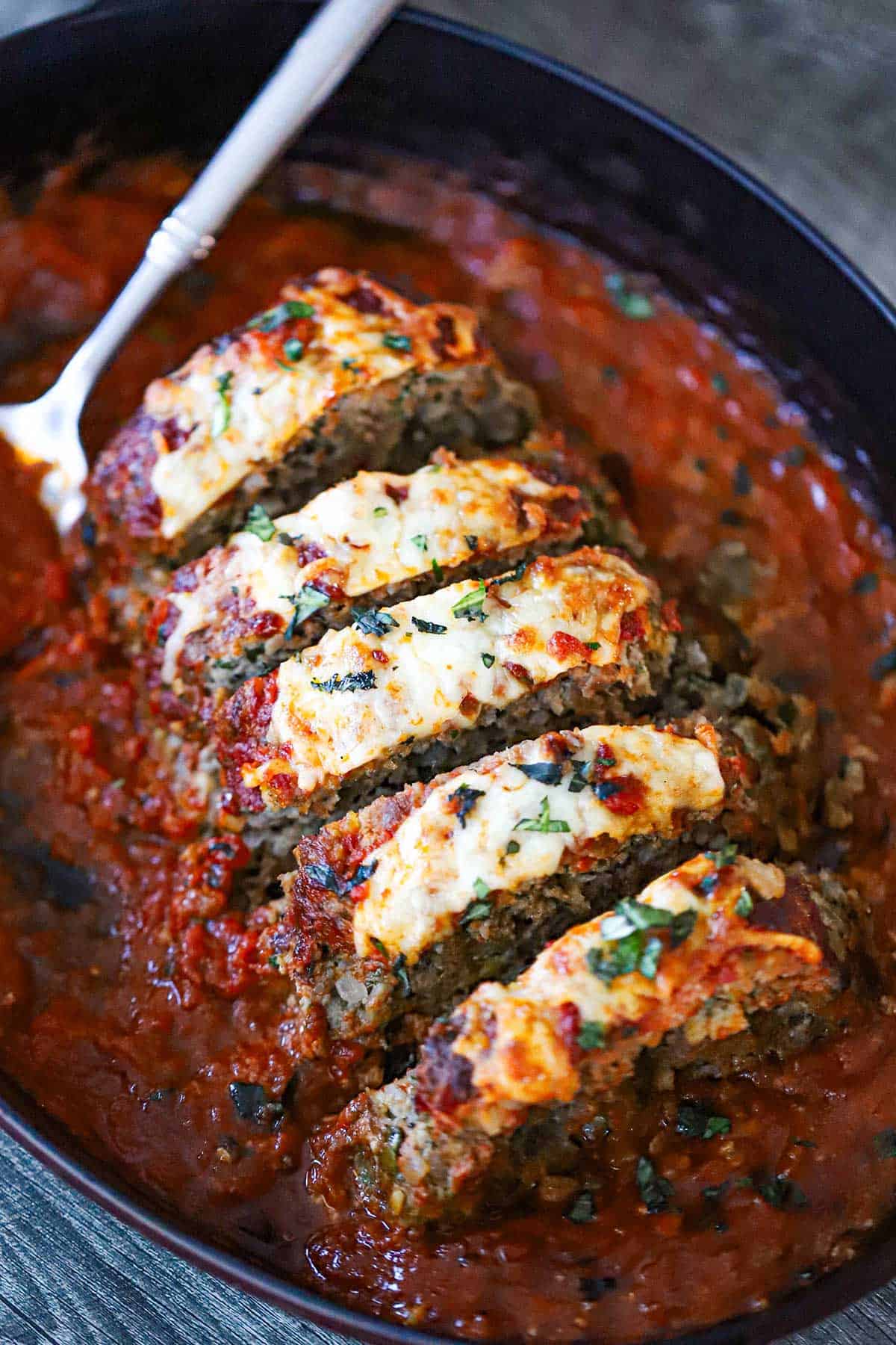 The Best Juicy Italian Meatloaf with Marinara Glaze cut into slices in an oval baking dish that is partially filled with marinara sauce.