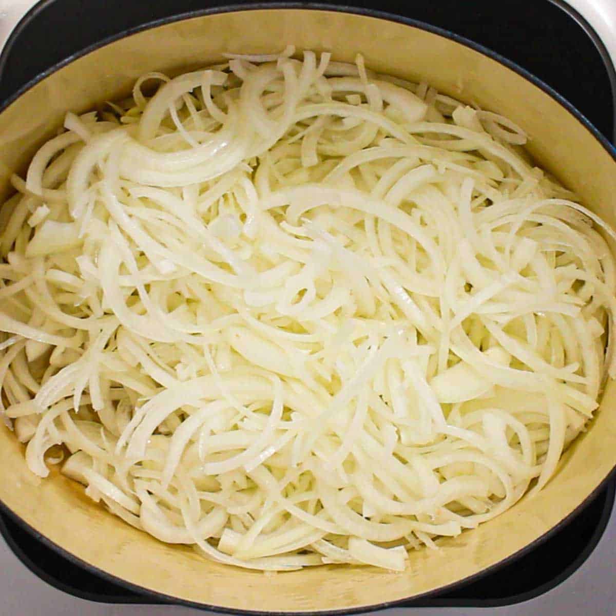 An overhead view of a large Dutch oven filled with sliced onions.