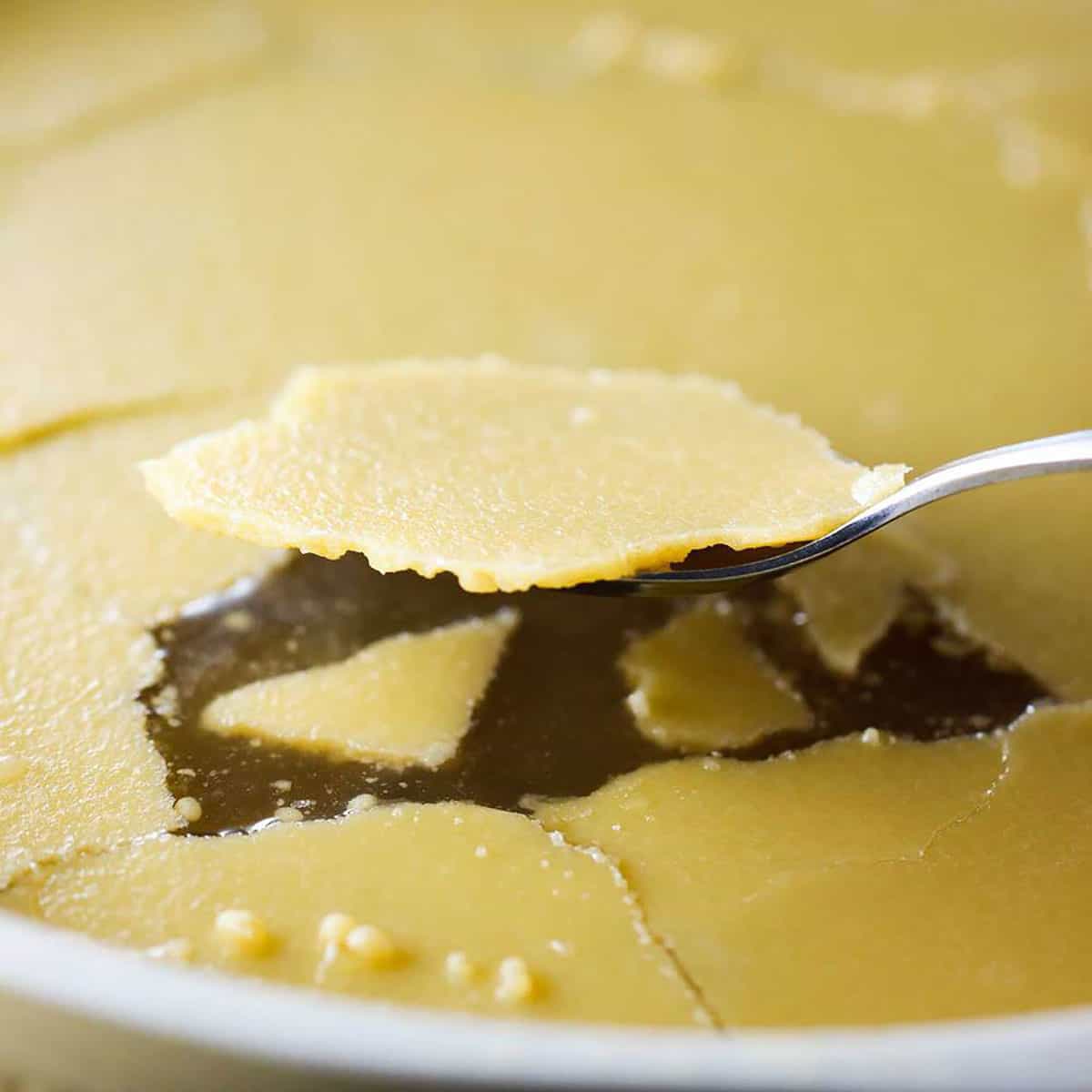 A spoon being used to scrape up congealed fat that has from on the surface of chilled beef stock in a stock pot.