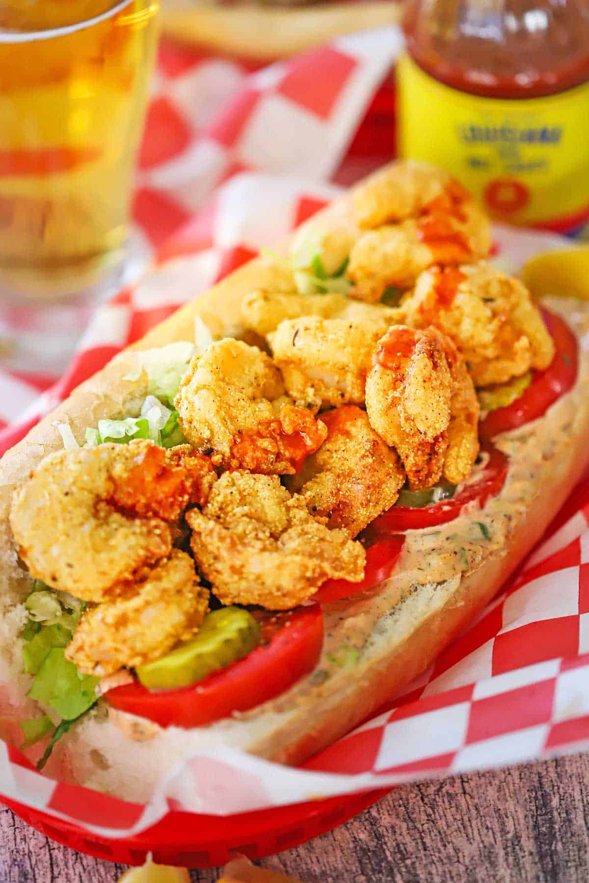 A close-up view of a New Orleans Fried Shrimp Po-Boy sandwich in a red plastic basket lined with red and white checkered wax paper.
