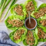 A circular white platter filled with P.F. Chang's Chicken Lettuce Wraps with a festive bowl filled with a zesty red sauce in the middle of the platter.