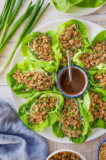 An overhead view of a circular white platter filled with P.F. Chang's Chicken Lettuce Wraps with a festive bowl filled with a zesty red sauce in the middle of the platter.