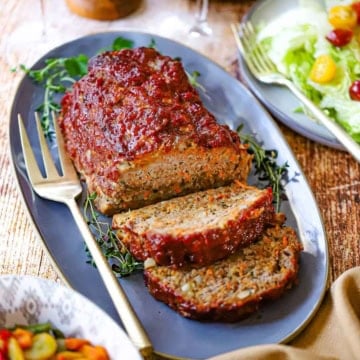 A close-up view of a juicy turkey meatloaf with two slices cut away all resting on an oval blue platter.