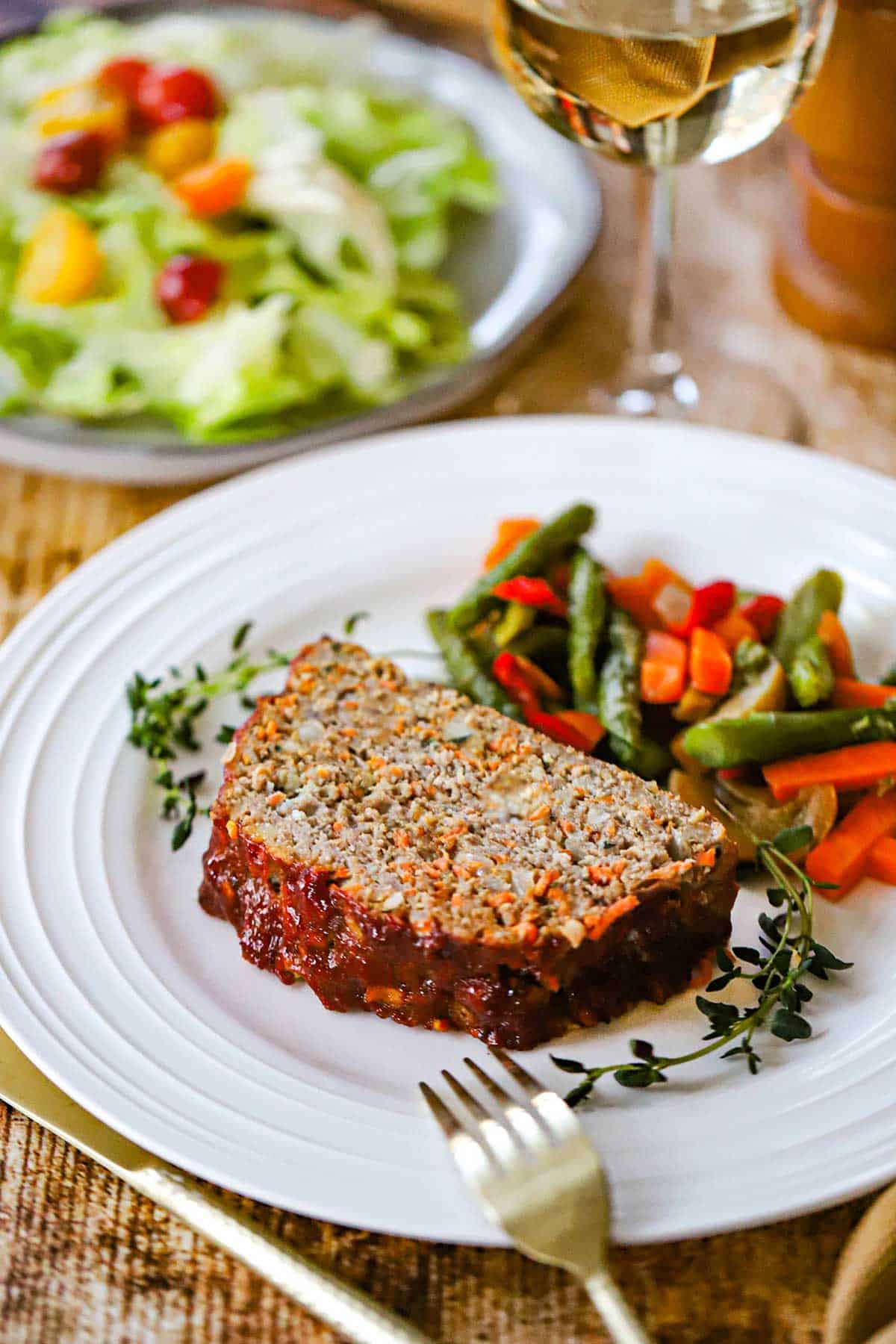 A thick slice of juicy turkey meatloaf resting on a white dinner plate with a pile of steamed vegetables next to it.