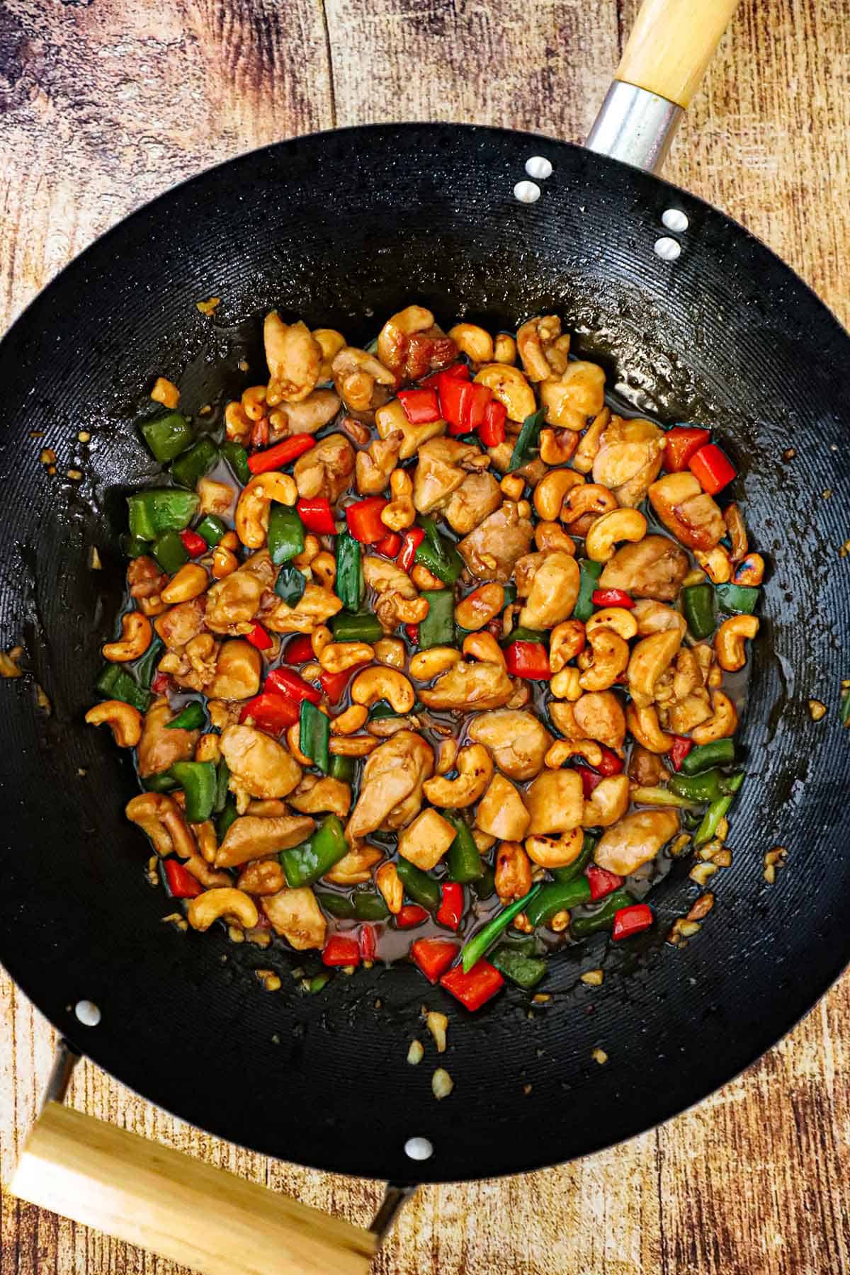 An overhead view of a large wok filled with freshly prepared cashew chicken garnished with chopped scallions.