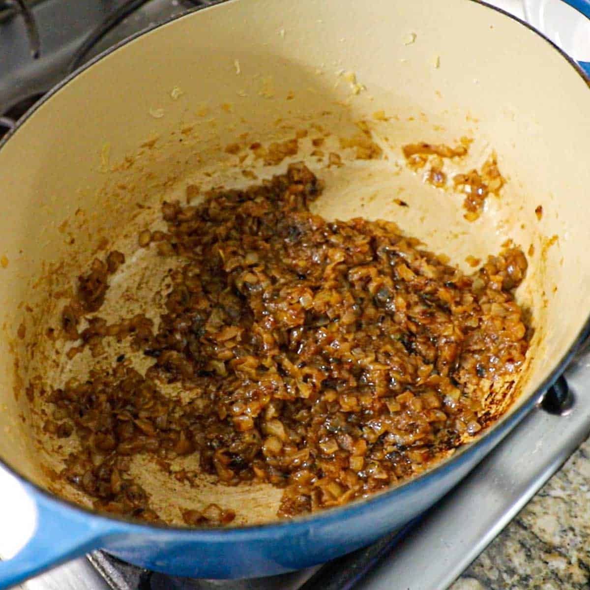 An overhead view of a large oval Dutch oven that has deeply caramelized chopped onions in the bottom of the pot.