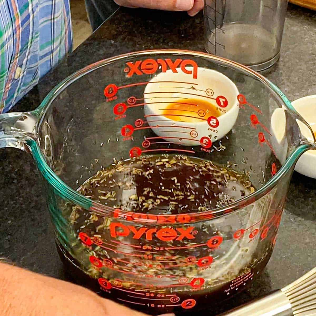 A close-up view of a 8-cup glass measuring cup filled with three cups of beef broth and dried herbs.
